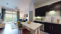 Located on Violet Crown Lane in Austin, Texas, this single-floor residence offers a thoughtfully designed layout that balances modern style with everyday functionality. The open-concept kitchen is a standout feature, outfitted with bold dark cabinetry, a classic white subway tile backsplash, granite-style countertops, stainless steel appliances, and under-cabinet lighting that creates a warm, inviting ambiance. A freestanding kitchen island with a quartz-style top provides additional prep space and casual seating, making it ideal for both cooking and entertaining. Wood-look flooring extends throughout the main living areas, lending a clean, cohesive aesthetic. The living room is bright and welcoming, with a ceiling fan, ample natural light, and sliding glass doors that open to a private balcony with outdoor seating — perfect for enjoying the Austin greenery. The bedroom is a serene retreat, featuring plush carpeting, large windows with views of lush surroundings, and generous space for furnishings. The full bathroom is elegantly finished with large-format marble-look tile flooring and a tub-shower combination, and connects directly to a spacious walk-in closet. Throughout the residence, a neutral color palette and high-quality finishes create a polished and comfortable living environment.