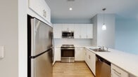 Located at 600 Crown Colony Dr in Quincy, Massachusetts, this single-floor unit offers a well-designed layout with modern finishes throughout. The kitchen is a standout feature, equipped with stainless steel appliances including a refrigerator, range, built-in microwave, and dishwasher. Crisp white cabinetry extends to the ceiling, providing ample storage, while light stone countertops and a peninsula with a sink add both functionality and style. Pendant lighting and light wood-style flooring complete the kitchen's contemporary aesthetic. The living area is bright and open, with large windows that allow natural light to fill the space and offer views of the surrounding community. Light wood-style flooring continues through the main living space, giving it a clean, cohesive look. The bedrooms feature soft carpeting and large windows that bring in additional natural light, creating comfortable, well-lit retreats. The bathroom is finished with light wood-style tile flooring, a warm-toned vanity with under-sink storage, a full tub and shower combination, and a large mirror. Soft blue-gray walls are consistent throughout the unit, lending a calm, neutral palette that ties the space together with a modern, inviting ambiance.