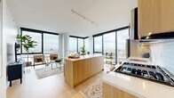 Located at 1475 N Kingsbury in Chicago, IL, this contemporary high-rise residence offers a refined modern living experience defined by clean lines, natural materials, and expansive city views. The open-concept living and kitchen area serves as the heart of the home, featuring light wood flooring, floor-to-ceiling black-framed windows on multiple sides, and abundant natural light throughout the day. The kitchen is appointed with warm wood cabinetry, a generous island with a white quartz countertop, and high-end appliances including a built-in gas cooktop and a statement range hood. The living area flows seamlessly from the kitchen, offering corner window views across the Chicago skyline. The primary bedroom is a serene retreat highlighted by a full wall of floor-to-ceiling windows with sweeping city views, light hardwood floors, and ample closet space. A second bedroom provides a quieter, well-appointed space with built-in closets. The bathrooms feature neutral tile flooring, wood-toned vanity cabinetry, and clean white surfaces. Track lighting and recessed fixtures provide versatile illumination throughout, while the consistent use of warm wood tones and white walls creates a cohesive, sophisticated aesthetic across the entire residence.