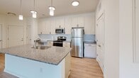 Located at 320 Fisher St in Charlottesville, Virginia, this single-floor residence offers a thoughtfully designed layout with modern finishes throughout. The kitchen is a standout feature, equipped with stainless steel appliances including a refrigerator, range, and over-the-range microwave. Light wood cabinetry, granite countertops, a subway tile backsplash, and a central island with a sink create a functional and stylish cooking space. Pendant lighting and recessed fixtures illuminate the area, while light wood-look flooring ties the space together seamlessly.

The living and dining areas benefit from large windows and a glass door that invite natural light and offer views of the surrounding landscaped grounds and walkways. The bedrooms feature plush carpeting, ceiling fans, and generous wall space, providing a comfortable and quiet retreat.

The bathrooms are well-appointed with granite-topped vanities and light wood cabinetry. One bathroom includes a dual-sink vanity and a soaking tub with shower combination, while another features a walk-in glass shower and an adjacent double-door closet. Light wood-look flooring continues throughout the bathrooms, reinforcing the cohesive aesthetic of the unit. Overall, the space presents a clean, contemporary design with an open and airy ambiance.