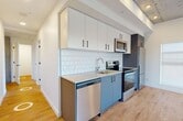 Located at 12322 102 Ave NW, this thoughtfully designed 3-bedroom, 1-bathroom unit offers a functional single-floor layout with contemporary finishes throughout. The kitchen is a standout feature, equipped with stainless steel appliances including a fridge, electric range, built-in microwave, and dishwasher. Two-tone cabinetry in white and slate blue pairs with a classic white subway tile backsplash, all set atop light hardwood flooring that flows consistently through the entire unit. An exposed concrete ceiling in the kitchen and hallway areas adds an industrial character that contrasts attractively with the clean white walls.

The three bedrooms are bright and simply designed, each benefiting from natural light through large windows that frame views of the surrounding neighbourhood. One bedroom features a built-in closet with rod storage. A dedicated hallway connects the rooms and conveniently houses a stacked washer and dryer unit. The bathroom is finished with clean white tile and a full shower/tub combination with matte black hardware accents. A separate closet provides additional storage. The overall ambiance is modern and clean, with an industrial-residential aesthetic defined by the interplay of concrete, white walls, and warm wood flooring.