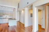 This contemporary two-story residence is defined by clean architectural lines, soaring double-height ceilings, and an open, airy layout that promotes seamless flow between living spaces. Rich hardwood flooring extends throughout the main level, reflecting abundant natural light that pours in through floor-to-ceiling windows and a large sliding glass door framing views of surrounding greenery.

The kitchen is a well-appointed space featuring light wood cabinetry that reaches toward the elevated ceiling, dark granite countertops, a striking geometric-patterned tile backsplash, and a full suite of stainless steel appliances including a refrigerator, range, built-in microwave, and dishwasher. A central island with matching granite provides additional prep and storage space.

The open-plan main level connects the kitchen to a generously sized living area, offering flexibility for various configurations. Recessed lighting and an accessible electrical panel are thoughtfully integrated into the layout. The second floor includes carpeted bedroom spaces with windows that bring in soft, diffused light. The bathroom is finished with neutral tile flooring, a tub-shower combination with subway tile surround, granite vanity, and brushed nickel fixtures. Throughout, the design emphasizes a minimalist modern aesthetic with a neutral, bright palette.