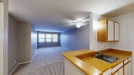 Located at 950 Village Green Ln in Waterford, Michigan, this one-bedroom, two-bathroom residence offers a practical and comfortable single-floor layout. The open-concept living and kitchen area is a central highlight, featuring a wraparound laminate breakfast bar that connects the kitchen to the spacious carpeted living room. The living room is brightened by a wide multi-panel window fitted with vertical blinds and is finished with a ceiling fan and light fixture overhead. The galley-style kitchen is equipped with wood-toned cabinetry, white appliances including a coil-top range and full-size refrigerator, a double sink, laminate countertops, and track lighting above. The generously sized bedroom features soft carpeting, neutral taupe walls, and a large window that draws in natural light. Two full bathrooms serve the residence — one featuring a tub/shower combo with clean white tile surround, and the other showcasing a marble-topped vanity with wood cabinetry, a lighted mirror, and tile flooring. A dedicated closet provides additional storage. The overall design is functional and bright, with consistent neutral tones and carpeted living spaces complemented by tile and wood-look flooring in the wet areas.