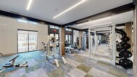 Located at 1033 East Sawmill Road in Flagstaff, Arizona, this two-floor fitness facility offers a comprehensive and thoughtfully designed workout environment spread across two generously sized levels. The space features a contemporary aesthetic defined by bold dark accent beams, warm wood-paneled columns, and multi-toned modular carpet tiles in shades of blue, gray, and green that lend a dynamic energy to the floors.

The lower level is anchored by soaring double-height ceilings that create an open, airy atmosphere. Large windows along the perimeter flood the space with natural light and provide views of the surrounding outdoor environment. A striking motivational mural serves as a focal point, reinforcing the facility's energetic character. This floor houses a robust selection of strength training equipment, including cable machines, weight benches, a power rack, and a well-stocked dumbbell rack, all reflected in wall-to-wall mirrors that enhance the sense of space.

The upper level, connected by a metal-railed mezzanine overlooking the floor below, is dedicated primarily to cardio training. A long row of treadmills, rowing machines, ellipticals, and StairMasters lines the space beneath recessed linear LED lighting. Ceiling fans provide additional comfort throughout. Together, the two floors form a cohesive, well-equipped fitness destination suited for a full range of training needs.