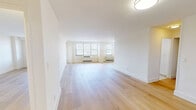 Located at 65-77 Prospect Street in downtown Stamford, Connecticut, this one-bedroom, one-bathroom residence offers a well-designed single-floor layout with a clean, modern aesthetic. The open living area is a standout feature, characterized by wide-plank light hardwood flooring, crisp white walls, and flush ceiling lighting that together create a bright and airy atmosphere. Multiple windows fitted with horizontal blinds allow natural light to fill the space throughout the day, while under-window HVAC units provide year-round climate control.

The generously proportioned bedroom continues the same hardwood flooring and neutral palette, offering a calm and flexible space. A dedicated closet provides practical storage. The bathroom is finished with classic white subway tile surrounding a full soaking tub and shower combination, complemented by a white vanity with brushed gold hardware, a mirrored medicine cabinet, and light tile flooring — delivering a timeless, clean look.

A connecting hallway links the main living area to the private rooms, creating a logical and efficient flow throughout the residence. The overall design emphasizes simplicity and functionality, making this Stamford residence a well-appointed option in a convenient urban location.