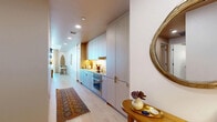 Located at 700 Broadway in Santa Monica, CA, this one-bedroom, one-bathroom residence offers a thoughtfully designed single-floor layout with a warm, modern aesthetic. The entry hallway sets an inviting tone with light wood flooring, recessed lighting, and a sleek galley-style kitchen featuring floor-to-ceiling custom cabinetry in a soft gray-wood finish, integrated appliances, and under-cabinet lighting that adds a refined glow. The living room is a standout space, highlighted by expansive floor-to-ceiling windows that flood the room with natural light and frame outdoor views of the Santa Monica skyline and surrounding greenery. Light hardwood floors and a clean, open layout give the living area a bright and airy feel. The bedroom offers a cozy, intimate atmosphere with textured accent walls, warm-toned ceiling details, and pendant lighting. Two closets provide ample storage. The bathroom is finished with polished marble tile from floor to ceiling, a spacious glass-enclosed walk-in shower with a built-in bench, and clean, minimalist fixtures. Throughout the residence, the interiors strike a balance between contemporary design and comfortable livability, making it a well-appointed home in the heart of Santa Monica.