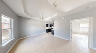 This single-story unit offers a well-organized layout across a modest but functional footprint, accommodating a combined kitchen and living area, one bedroom, one bathroom, and a closet. The interior is finished with large-format light ceramic tile flooring throughout, providing a clean, cohesive look across all rooms.

The living and dining area greets residents at entry through an arched front door, featuring a tray ceiling detail accented by a chandelier-style light fixture. Cool gray walls and a window allowing natural light give the space an open, airy feel.

The galley-style kitchen runs parallel along two walls, outfitted with dark espresso cabinetry contrasting against light countertops and a double stainless steel sink. A white refrigerator and gas range provide full appliance functionality, with upper cabinets offering ample storage on both sides of the corridor layout.

The bedroom is a well-proportioned retreat highlighted by a tray ceiling with a ceiling fan, a window with exterior views, and the same consistent tile flooring and gray wall tones found throughout the unit.

The bathroom includes a vanity with a light countertop, toilet, and direct sightline to the kitchen, efficiently positioned for accessibility. A dedicated closet completes the layout, supporting practical everyday storage needs.