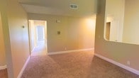 This single-floor space presents a straightforward and functional layout. The main living area features wall-to-wall carpet in a warm beige tone, contributing to a comfortable and understated atmosphere. Neutral-colored walls are accented by clean white baseboards, creating a simple yet cohesive aesthetic throughout. A textured ceiling adds subtle visual interest overhead, while a ceiling vent ensures climate control throughout the space. A built-in niche on one wall offers a dedicated spot for display or storage, adding a minor architectural detail to the otherwise open layout. A hallway visible from the main area connects to additional rooms, suggesting a practical flow through the space. The overall ambiance is clean and move-in ready, providing a neutral canvas well-suited for personalization. The understated design and consistent finishes throughout make this a versatile space adaptable to a variety of furnishing styles and functional needs.