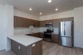 This 1-bedroom, 1-bathroom unit at 703 N Main St in Meridian, Idaho, showcases a contemporary design with clean lines, light-toned luxury vinyl plank flooring, and a bright, open layout throughout. The kitchen is a standout feature, outfitted with warm wood-grain cabinetry extending to the upper walls, a marble-style tile backsplash, white quartz countertops, and a full suite of stainless steel appliances including a range, microwave, dishwasher, and refrigerator. A peninsula counter provides additional prep space and defines the transition into the open living area.

The living space benefits from a wall-mounted mini-split HVAC unit and a sliding glass door that opens onto a private balcony with decorative metal railing, allowing for natural light and outdoor views. The bedroom is a comfortable, well-lit room with its own mini-split unit, a window overlooking the surrounding area, and access to a closet.

The bathroom features light wood-grain cabinetry, a wide white quartz vanity with a single sink, a large mirror with bar lighting, and a full soaking tub and shower combination with white tile surround. The consistent use of wood-toned finishes and neutral tones throughout creates a cohesive, modern aesthetic.