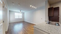 This single-floor unit offers a thoughtfully designed open-concept layout that seamlessly connects the living, dining, and kitchen areas. The living space is finished with warm hardwood-style flooring and is bathed in natural light from a large window, while a ceiling fan adds comfort overhead. Track lighting further illuminates the space, highlighting the clean, neutral-toned walls throughout.

The kitchen is a standout feature, boasting rich dark cabinetry paired with light granite countertops that extend to a peninsula with a built-in sink — ideal for both meal preparation and casual dining. Black appliances, including a range and refrigerator, complement the cabinetry, while ample upper and lower cabinet storage ensures plenty of functionality.

The entryway area provides practical access to multiple doors, including closet and unit entry, maintaining an organized and efficient flow throughout the space. The bedroom is carpeted for added comfort, featuring a ceiling fan and a generously sized window that invites natural light and outdoor views. Neutral wall tones across all rooms create a cohesive, versatile palette ready for personalization. Overall, this space delivers a clean, modern aesthetic with practical finishes designed for everyday living.