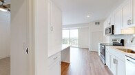 This well-appointed 1-bedroom unit offers a thoughtfully designed single-floor layout that maximizes functionality and comfort. The open-concept kitchen and living area serves as the heart of the space, featuring warm hardwood-style flooring, recessed lighting, and a floor-to-ceiling sliding glass door that opens onto a private balcony with expansive views of the surrounding landscape. The kitchen is outfitted with stainless steel appliances, including a range with over-the-range microwave, white shaker-style cabinetry with brushed nickel hardware, a light subway tile backsplash, and a peninsula with quartz countertops that provides additional prep and dining space. Natural light flows generously throughout the main living area, enhancing the bright, airy atmosphere created by the crisp white walls and clean-lined design. The bedroom is comfortably sized, featuring plush carpeting and neutral tones that offer a calm retreat. A dedicated closet provides practical storage. The bathroom includes a white vanity with ample cabinet storage, a framed mirror, and a walk-in shower. The unit's modern aesthetic, quality finishes, and functional layout make it a highly livable and attractive space.