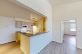 Located at 100 Hilltop Dr in Walpole, MA, this one-bedroom, one-bathroom unit offers a well-designed single-floor layout that makes efficient use of its space. The open-concept kitchen and living area serves as the heart of the unit, featuring a peninsula with granite-style countertops, light wood cabinetry, track lighting, and white appliances including a range, microwave, and refrigerator. The kitchen flows seamlessly into the living area, which is finished with light hardwood-style flooring that extends throughout the unit. The bedroom is a standout feature, showcasing dramatic vaulted ceilings with a textured finish and a distinctive arched window that frames natural light beautifully, creating an airy and spacious feel. A dedicated closet with bi-fold doors provides convenient storage. The bathroom is clean and functional, featuring a full tub-shower combo with white tile surround accented by a neutral decorative band, complemented by chrome fixtures and wood-look flooring. A dedicated entrance and additional closet space complete the layout. The unit's bright, neutral palette and architectural details such as the vaulted ceiling make it a comfortable and practical living space.