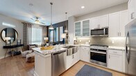 Located at 6611 E Mayo Blvd in Phoenix, Arizona, this well-appointed single-floor residence offers a cohesive blend of modern design and functional living. The open-concept kitchen is a standout feature, showcasing crisp white shaker cabinetry with frosted glass upper panels, striking granite countertops, a farmhouse-style stainless steel sink, and a full suite of stainless steel appliances including a gas range, built-in microwave, refrigerator, and dishwasher. A decorative arabesque tile backsplash adds texture, while pendant lighting illuminates the kitchen island with bar seating. Light hardwood flooring flows throughout the main living areas, extending into a bright dining nook bathed in natural light from large floor-to-ceiling windows and a glass door. The bedroom is a serene retreat highlighted by a bold teal accent wall, plush carpeting, a ceiling fan, and generous natural light. A spacious walk-in closet provides extensive built-in shelving and hanging storage. The bathroom features a long dual-sink vanity with dark granite countertops, white cabinetry, large-format tile flooring, and a separate water closet. A thoughtfully designed built-in desk nook with upper cabinetry and a tile backsplash adds a versatile workspace. Throughout the residence, neutral tones and carefully considered finishes create a polished, contemporary ambiance.