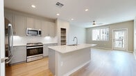 Located on East Camelback Road in Phoenix, this one-bedroom, one-bathroom unit offers a thoughtfully designed open-concept layout with modern finishes throughout. Light wood-style flooring flows seamlessly through the main living areas, complementing the neutral color palette that gives the space a clean, contemporary feel.

The kitchen serves as a central hub, anchored by a large island with a white quartz countertop, an integrated sink with a modern gooseneck faucet, and seating potential. Gray shaker-style cabinetry lines the walls, paired with a white subway tile backsplash, under-cabinet lighting, and a full suite of stainless steel appliances including a gas range, microwave, and refrigerator. An open shelving nook adds additional storage and visual interest.

The living area receives natural light through a large window and features a ceiling fan overhead. A glass-panel door leads to an exterior view of the surrounding development. The bedroom is carpeted and benefits from natural light, while the dedicated closet provides well-organized storage with multiple hanging rods and shelving.

The bathroom offers a spacious, elongated layout with a soaking tub surrounded by large-format gray tile, a gray vanity with a white countertop, and light wood flooring that continues from the main living areas, tying the space together cohesively.