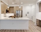 This thoughtfully designed 570-square-foot, one-bedroom, one-bathroom apartment offers a modern aesthetic with high-quality finishes throughout its single floor. The open-concept kitchen serves as the centerpiece of the living space, featuring flat-front cabinetry in a warm wood tone, white quartz countertops, a large center island with an undermount sink, and a full suite of stainless steel appliances including a refrigerator with ice maker, range, microwave, and dishwasher. Globe pendant lights add a contemporary touch above the island. A built-in desk nook provides a practical workspace near the entryway. Light wood-look luxury vinyl plank flooring flows seamlessly throughout the unit, creating a cohesive and clean look. The 140-square-foot primary bedroom is bright and airy, with a ceiling fan, natural light from a large window with roller shade, and direct access to the bathroom and closet. The bathroom makes a bold design statement with navy blue vanity cabinetry, a dual-sink white quartz countertop, matte black hardware and fixtures, an LED-lit mirror, and a tiled soaking tub with matching wall tile. Crisp white walls and clean-panel interior doors complete the modern, minimalist character of this well-appointed unit.