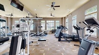 Located at Bristol Village in Midlothian, Virginia, this fitness center offers a comprehensive workout environment within a well-designed, single-floor layout. The space is thoughtfully appointed with warm neutral tones, taupe walls, and a patterned carpet flooring that adds texture underfoot. Elevated ceilings with dual ceiling fans promote airflow throughout, while recessed lighting ensures the room is consistently well-lit.

Large multi-pane windows line the walls on multiple sides, flooding the interior with natural light and providing pleasant views of the surrounding greenery. The abundance of natural light creates an open, energizing atmosphere ideal for exercise.

The fitness center is fully equipped to support a range of workout routines. Cardio equipment includes multiple treadmills, elliptical trainers, and a stationary cycle, all positioned to take advantage of the natural light and outdoor views. The strength training area features a multi-station cable machine, a weight bench with barbell rack, and a three-tier dumbbell rack stocked with a full range of free weights. Wall-mounted mirrors expand the sense of space and allow users to monitor their form during workouts. Wall-mounted televisions provide entertainment options. The space also includes sanitation stations and clearly defined entry doors, contributing to a clean and organized environment.