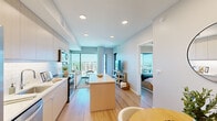 Located in the heart of downtown Raleigh, this contemporary 2-bedroom, 1-bathroom residence offers a well-designed open-concept layout with refined modern finishes throughout. Light wood-tone flooring runs seamlessly across the entire unit, complementing the clean, neutral color palette.

The kitchen is a standout feature, equipped with stainless steel appliances, light gray flat-front cabinetry, white quartz countertops, a classic subway tile backsplash, and a center island that provides additional prep space and flows naturally into the dining area. The dining space is accented by a round wood table and a circular wall mirror, adding warmth and dimension to the open layout.

The living room benefits from floor-to-ceiling windows that flood the space with natural light and frame impressive elevated views of the Raleigh skyline and surrounding cityscape. A sage green accent wall adds a distinctive touch to the living area.

The primary bedroom is generously proportioned, featuring large sliding glass doors that open to a private balcony with panoramic city views. The second bedroom is cozy and well-appointed with neutral tones and tasteful décor.

The bathroom features wood-toned cabinetry, a white quartz vanity, and a full tub-shower combination with earthy tile surround, offering a clean and functional design.