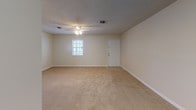This single-floor space offers a straightforward and functional layout, as seen in the 3D floor plan, with distinct areas for living, sleeping, cooking, and bathing. The kitchen is efficiently designed with warm honey-toned wood cabinetry lining both walls, dark speckled countertops, light tile flooring, and white appliances including a full-size refrigerator and built-in dishwasher, providing ample storage and workspace for everyday use.

The living area is generously sized, featuring neutral beige carpeting, a ceiling fan with light fixture, a textured ceiling, and a window that allows natural light to filter in. A secondary carpeted room serves well as a bedroom or flexible space, also benefiting from a window with blinds and the same textured ceiling treatment. An additional carpeted room with smooth walls and a textured ceiling provides further versatility.

The bathroom is cleanly appointed with tile flooring, a full-size tub and shower combo, a toilet, and a wood-toned overhead storage cabinet, keeping essentials within easy reach. Consistent neutral wall tones, white trim, and carpeted floors throughout lend the space a cohesive and understated character.