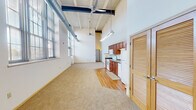 Located at 2130 South Ave in La Crosse, Wisconsin, this two-floor loft-style space showcases an impressive industrial-inspired design with soaring ceilings, exposed ductwork, and beam detailing throughout the main level. The open-concept living and kitchen area is defined by a seamless blend of warm hardwood flooring and plush carpeting, creating distinct functional zones within a single expansive space. Large multi-pane windows line the walls, inviting abundant natural light and offering views of the surrounding neighborhood. Ceiling fans and industrial-style light fixtures complement the converted building aesthetic.

The kitchen features rich cherry wood cabinetry, a full suite of white appliances including a range and microwave, and ample counter space beneath soaring ceilings that amplify the sense of volume. A louvered door provides access to additional storage or utility space nearby.

Both bathrooms are finished with warm hardwood flooring, cherry wood vanities, and full tub-shower combinations. The upper floor offers carpeted rooms with multiple windows, painted brick accent walls, and structural columns that add to the space's character. Storage is well-accommodated with a generously sized walk-in closet featuring wire shelving on multiple walls, as well as additional closet space with wire rod systems throughout.
