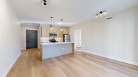 This thoughtfully designed 2-bedroom, 2-bathroom residence in Brookfield, CT offers a clean, modern aesthetic carried consistently throughout its single-floor layout. Light-toned hardwood flooring flows seamlessly across the open-concept living, dining, and kitchen area, creating a bright and cohesive atmosphere. The kitchen is a standout feature, showcasing light wood cabinetry, white quartz countertops, a white subway tile backsplash, and a full suite of stainless steel appliances. A central island with a matte black sink and pendant globe lighting above serves as both a functional workspace and a natural gathering point. The living area is generously proportioned and connects directly to an outdoor space via a black-framed glass sliding door. Both bedrooms are well-lit, with black-framed windows inviting abundant natural light and outdoor views. The primary bedroom is spacious with a dedicated closet. Each bathroom features light wood vanities with white countertops, large-format tile flooring, and glass-enclosed walk-in showers with floor-to-ceiling tile surround. A dedicated in-unit laundry room with a full-size washer and dryer adds everyday convenience. The space offers a fresh, move-in-ready feel with a neutral palette and modern hardware throughout.
