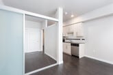 This single-floor residence showcases a contemporary design with dark hardwood flooring running consistently throughout the space. The galley-style kitchen is well-appointed with light wood cabinetry, dark countertops, and a full suite of stainless steel appliances, including an electric range, over-the-range microwave, dishwasher, and refrigerator. A white subway tile backsplash with a contrasting dark accent stripe adds a modern detail, while a stainless steel sink is positioned beneath recessed lighting. The kitchen opens toward a bright living area featuring a large floor-to-ceiling window fitted with horizontal blinds, allowing ample natural light and views of the surrounding neighborhood.

The bedroom is a well-proportioned room with neutral-toned walls, dark hardwood floors, and a sliding mirrored closet that enhances the sense of space. A window with horizontal blinds provides natural light. The bathroom is straightforward in design, featuring a soaking tub with shower surround, a wall-mounted grab bar, and neutral gray walls. The 3D floor plan reveals a compact, efficiently arranged layout with a clearly defined corridor connecting the kitchen, living area, bedroom, and bathroom.