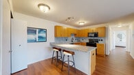 This single-floor residence offers a thoughtfully designed layout that balances functionality with comfort. The open-concept kitchen is a standout feature, showcasing warm honey-toned wood cabinetry, a granite tile backsplash, and granite countertops that extend across a peninsula island with bar seating for two — ideal for casual dining or entertaining. Black appliances, including a range, over-the-range microwave, and dishwasher, complement the kitchen's modern aesthetic. A convenient in-unit stacked washer and dryer is tucked neatly into a closet just off the kitchen area.

Rich hardwood-style flooring flows throughout the main living spaces, lending warmth and continuity. The living room is bright and open, featuring large sliding glass doors with vertical blinds that invite natural light and provide outdoor access.

The primary bedroom is generously sized, featuring hardwood-style flooring and a direct en-suite bathroom connection. The en-suite bath is finished with a granite-topped vanity, warm wood cabinetry, and tile flooring. A second bedroom offers a large closet and a window with outdoor views. A second full bathroom with a tub/shower combination and tile flooring completes the layout, making this a practical and well-finished living space.