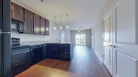This single-story, 2-bedroom, 2-bathroom residence offers a thoughtfully designed open-concept layout that maximizes its comfortable footprint. The kitchen serves as a central hub, featuring dark espresso cabinetry extending to the ceiling, granite-style countertops, black appliances including a refrigerator, range, microwave, and dishwasher, and a peninsula with pendant lighting overhead. Hardwood-style flooring flows throughout the kitchen and living areas, creating a cohesive, easy-to-maintain surface. The living room benefits from natural light streaming through a large sliding glass door fitted with vertical blinds, and a ceiling fan provides additional comfort. Both bedrooms are carpeted and include ceiling fans, with each room accessing a dedicated walk-in closet equipped with wire shelving systems. The primary bedroom connects directly to its en-suite bathroom, which features dark vanity cabinetry with granite-style counters, hardwood-style flooring, a shower, and direct access to a spacious walk-in closet. The second bedroom is similarly well-sized with its own walk-in closet. The overall aesthetic is consistent throughout, with neutral tones and clean finishes.