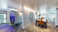Located at 37 8th Ave in Oakland, CA, this thoughtfully designed single-floor amenity space offers a sophisticated blend of collaborative and private work environments. The open layout is anchored by a stylish lounge area furnished with a plush sectional sofa, accent pillows, and a minimalist coffee table, complemented by curated wall art that adds a vibrant, creative energy to the space.

A standout feature is the freestanding oval pod workstation, bathed in ambient purple lighting, offering an intimate and focused work setting within the open floor plan. Adjacent to the lounge, a formal conference area provides a dark-topped table with warm amber leather chairs, ideal for meetings and collaboration. Floor-to-ceiling glass partitions divide the space into distinct zones while maintaining visual openness and allowing natural light to flow throughout.

A glass-enclosed private meeting room with a round table and modern chairs offers additional privacy for smaller gatherings. Large sliding glass doors open to an outdoor terrace, inviting natural light and outdoor views into the interior. Patterned carpeting, recessed and cove lighting, and neutral gray walls unify the space with a contemporary, professional aesthetic. Lush indoor plants add a refreshing natural element throughout.