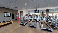 Located at 5445 Lankershim Blvd in North Hollywood, this fitness center is a thoughtfully designed, single-floor facility that offers a comprehensive workout environment. The space features a suspended tile ceiling with recessed lighting throughout, creating a bright and functional atmosphere complemented by large windows along one wall that flood the interior with natural light and provide views of an outdoor terrace area.

The cardio zone is equipped with multiple treadmills arranged in a row, accompanied by a wall-mounted flat-screen television for entertainment during workouts. Nearby, a dedicated area houses stability and medicine balls, along with a Pilates reformer, catering to flexibility and core training. The strength training section features a variety of cable machines, weight benches, and free-weight stations, all positioned on protective floor matting.

The facility's color palette combines warm yellow accent walls with neutral gray tones, giving it a modern and energizing aesthetic. Motivational fitness photography decorates the walls, adding to the gym's active atmosphere. A water cooler station and accessible restrooms are conveniently located within the space. Full-length mirrors in the cardio area enhance the sense of openness. The layout is spacious and well-organized, ensuring ease of movement between equipment zones.