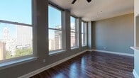 This one-bedroom, one-bathroom residence in downtown Memphis, TN offers a well-designed layout that maximizes both comfort and style. The living area is an immediate standout, featuring a row of large, tall double-hung windows that frame sweeping views of the Memphis skyline and flood the room with abundant natural light. Dark-stained hardwood flooring runs throughout, adding warmth and a polished aesthetic, while neutral gray walls provide a clean, versatile backdrop. A ceiling fan keeps the living space comfortable year-round. The bedroom continues the same design language, with corner windows on two walls offering additional city views and generous natural light, creating an airy and bright retreat. The kitchen is outfitted with white shaker-style cabinetry, light stone countertops, and stainless steel appliances, including a full-size refrigerator. A built-in pantry cabinet provides ample storage. The bathroom features wood-look vinyl flooring, a white vanity with dark countertop, a well-lit mirror, and a clean, functional layout. Throughout the unit, crisp white trim and baseboards provide a sharp contrast to the warm flooring tones, giving the space a cohesive, modern-meets-classic character well-suited to urban living in Memphis.