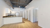 Located at 50 Prince Street in Rochester, NY, this one-bedroom, one-bathroom unit offers a modern industrial aesthetic with thoughtful finishes throughout. The open-concept living, dining, and kitchen area forms the heart of the space, anchored by soaring ceilings with exposed ductwork, steel beams, and track lighting that lend a contemporary loft character. Light wood-tone flooring runs throughout, creating warmth and visual continuity. The kitchen is well-appointed with white shaker cabinetry, dark granite countertops, a peninsula with an undermount sink, and a full suite of stainless steel appliances including a refrigerator, range, microwave, and dishwasher. Large floor-to-ceiling windows and a glass-panel entry door in the living area flood the space with natural light and offer open views of the streetscape. The bedroom is a well-proportioned, quiet retreat with clean white walls and wood flooring. Two closets provide generous storage. The bathroom features white cabinetry, a dark granite vanity top, a large mirror, and a drop ceiling with recessed lighting. A hallway connects the private areas to the main living space, completing this efficient and stylish urban residence.