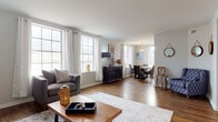 This well-appointed one-bedroom, one-bathroom unit is laid out across a single floor, offering a thoughtfully designed open-concept living and dining area. Rich hardwood floors extend throughout the main living spaces, complementing the neutral, light-toned walls that create a clean and welcoming atmosphere.

The living area is generously sized, accommodating a full seating arrangement with ease, and benefits from multiple large double-hung windows dressed with white curtain panels that invite ample natural light. A dedicated dining nook sits adjacent to the living space, featuring its own window and a pendant light fixture overhead, with direct sightlines into the kitchen.

The kitchen is efficiently designed with granite countertops, white cabinetry, tile flooring, and stainless steel appliances including a range and over-the-range microwave. A window above the counter provides additional natural light.

The bedroom is comfortably sized, featuring hardwood floors, a window with outdoor views, and a closet with built-in shelving. An additional closet is accessible from the living area, offering extra storage.

The bathroom is finished with marble-style large-format wall tiles surrounding the soaking tub, coordinating tile flooring, a pedestal sink, and a frosted window for natural light and privacy.