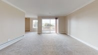 Located along Shoreline Drive in Alameda, California, this single-floor residence offers a thoughtfully laid-out living space with a clean, neutral aesthetic throughout. Crown molding adds a refined architectural detail to the main living and bedroom areas, which feature plush wall-to-wall carpeting underfoot. The spacious living area is anchored by a sliding glass door that opens to an outdoor balcony, allowing natural light to fill the room and providing views of the surrounding greenery. A ceiling fan enhances comfort in the adjoining area. The galley-style kitchen is well-equipped with warm-toned wood cabinetry, granite-look countertops, stainless steel appliances including a refrigerator, electric range, microwave, and dishwasher, and tile flooring. The bedrooms are generously sized, each featuring windows that bring in natural light, open closets with shelving, and baseboard heating. The primary bedroom includes an en-suite bathroom and closet access. Two bathrooms serve the residence: one features a combined tub and shower with sliding glass doors, a wood vanity with granite-look countertop, and tile flooring, while the second offers a standalone shower with a glass door. This residence presents a comfortable and functional layout in a well-maintained setting.