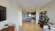 This single-floor residence offers a thoughtfully designed open-concept layout that seamlessly connects the kitchen, dining, and living areas. The kitchen is outfitted with dark wood cabinetry, stainless steel appliances including a French door refrigerator, electric range, built-in microwave, and dishwasher, all complemented by a classic white subway tile backsplash and light countertops. A compact dining table with bar-height seating sits adjacent to the kitchen, creating a functional everyday dining space. The living area is bright and welcoming, featuring light hardwood-style flooring, neutral-toned walls, and sliding glass doors that open to a private balcony with outdoor views and abundant natural light. The bedroom is a tranquil retreat with plush carpeting, a tufted upholstered headboard, dual nightstands, and a window dressed with plantation shutters that allow for natural light control. The bathroom features a dark wood vanity with a white stone countertop, a tub-shower combination with a tiled surround, and warm wall sconce lighting. Track lighting throughout the main living areas adds a modern touch, and the overall design palette of warm neutrals and contemporary fixtures creates a cohesive, inviting ambiance.