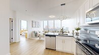 Located at 855 Main St in Bridgeport, CT, this modern residence offers a thoughtfully designed open-concept layout with 1 bedroom and 2 bathrooms. Light hardwood flooring runs throughout, complementing the bright, white interior and creating a clean, contemporary aesthetic.

The kitchen and living area flow seamlessly together, anchored by large floor-to-ceiling windows that flood the space with natural light and frame panoramic views of the Bridgeport skyline. The kitchen features white shaker cabinetry with gold hardware, dark granite countertops, a dark tile backsplash, stainless steel appliances including a dishwasher and refrigerator, and a peninsula ideal for dining or casual entertaining. A sculptural ring pendant light adds a modern design touch overhead.

The spacious primary bedroom is a bright retreat, wrapped in expansive corner windows offering sweeping city and waterfront views. It includes ample closet space and a serene, airy ambiance enhanced by natural light throughout the day.

The bathrooms are finished in clean white tile with matte black fixtures, offering a sleek, modern contrast. Throughout the residence, the generous windows not only maximize light but also provide a strong visual connection to the vibrant Bridgeport cityscape below.