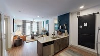 This single-floor residence offers a thoughtfully designed open-concept layout that seamlessly connects the kitchen, dining, and living areas. The kitchen is a standout feature, equipped with stainless steel appliances including a refrigerator, range, and microwave, complemented by dark shaker-style cabinetry, a subway tile backsplash, and a quartz-topped island with an undermount sink and bar seating. A sliding barn door adds a contemporary touch. The living area is bright and welcoming, featuring wood-style plank flooring, a ceiling fan, and large windows dressed with patterned drapes that invite natural light. A bold teal accent wall provides a striking visual anchor to the open space. The bedroom is carpeted for comfort, highlighted by a textured feature wall, a ceiling fan, and a generously sized window with exterior views. Both bathrooms are finished consistently with dark cabinetry, quartz countertops, wood-style flooring, and full tub-shower combinations with white subway tile surrounds. Open shelving provides additional storage in each bathroom. Throughout the residence, a cohesive modern-eclectic design palette ties each space together with vibrant accent colors and contemporary finishes.