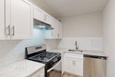 Located at 6166 Leesburg Pike in Falls Church, Virginia, this two-bedroom, two-bathroom residence offers a well-organized single-floor layout with a clean, modern aesthetic throughout. The open living room is bathed in natural light through large windows fitted with vertical blinds, and features light-toned hardwood-style flooring that extends across the main living areas, creating a cohesive and airy feel. The updated kitchen is a standout feature, showcasing white shaker cabinetry, granite-style countertops, a classic white subway tile backsplash, and stainless steel appliances including a gas range, dishwasher, and range hood. The primary bedroom is generously proportioned and connects to the hallway with convenient closet access. The second bedroom features plush carpeting and a window that allows ample natural light. Both bathrooms are finished with white vanities, granite-style countertops, brushed nickel fixtures, tiled tub-shower combinations, and tile wainscoting. A dedicated laundry area houses a stacked washer and dryer unit, adding practical convenience. Two hallways and two closets contribute to efficient storage and circulation throughout the home. The neutral color palette and updated finishes lend the space a fresh, move-in-ready character.