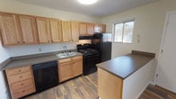 This single-floor unit offers a practical and well-organized layout designed for comfortable everyday living. The kitchen serves as a functional centerpiece, featuring warm honey-toned oak cabinetry that extends along the full length of the wall, providing generous storage space. Black appliances — including a gas range, dishwasher, and refrigerator — complement the neutral countertops, while durable wood-look flooring runs throughout the kitchen and adjacent areas. A peninsula counter adds additional prep and dining space, and a window above the sink brings in natural light with views of the surrounding neighborhood.

The bedrooms are carpeted and finished with neutral walls, creating a calm and restful atmosphere. Each bedroom benefits from windows that allow natural light to filter in. One bedroom features a sliding-door closet with built-in shelving and a rod for hanging storage, along with a sliding glass door that opens to an outdoor view. Additional bedroom spaces offer a similarly clean and open feel.

The bathroom is straightforward and well-maintained, featuring a full-size soaking tub with an integrated surround that includes built-in shelving, paired with a shower rod. The overall layout of the unit, as seen in the dollhouse view, presents a cohesive and efficiently arranged single-level floor plan.