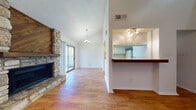 This two-floor residence offers a well-organized layout with warm hardwood-style flooring extending throughout both levels. The main living area serves as the heart of the home, highlighted by a striking floor-to-ceiling stone fireplace with a wooden mantel and accent panel, vaulted ceilings, and a classic chandelier. A sliding glass door fills the space with natural light and provides access to an outdoor area. The open-concept design connects the living room to the kitchen via a raised breakfast bar with overhead track lighting. The galley-style kitchen features white cabinetry, white appliances including a range, refrigerator, and dishwasher, and a double sink — all set against clean countertops and continued hardwood-style flooring. The upper level includes a loft-style room with sloped ceilings, offering a versatile and airy space. Additional rooms include well-sized bedrooms, one featuring a ceiling fan and light fixture, and a walk-in closet with built-in shelving and dual hanging rods. Two full bathrooms are present — one with a tub/shower combo and white cabinetry, and another with a vanity, medicine cabinet, and tub/shower. Textured ceilings and neutral white walls provide a clean, move-in-ready aesthetic throughout.