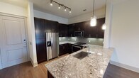 This single-floor residence offers a well-appointed layout that balances modern design with functional living spaces. The kitchen serves as a focal point, showcasing rich dark cabinetry that extends floor to ceiling, providing generous storage throughout. A large granite island with an undermount sink anchors the space, complemented by matching granite countertops along the perimeter. The subway tile backsplash in a soft sage-gray tone adds texture, while stainless steel appliances — including a French door refrigerator with ice maker, electric range, and built-in microwave — complete the contemporary aesthetic. Pendant lighting and track lighting illuminate the kitchen effectively.

The living area features warm hardwood flooring and leads to a set of French doors opening onto a private balcony, bringing in natural light and outdoor views. A ceiling fan with light fixture adds comfort to the space.

The bedroom is carpeted for warmth and comfort, fitted with a ceiling fan and a window overlooking the exterior. A spacious walk-in closet with multiple shelving rods and carpet flooring offers substantial storage capacity.

The bathroom features an elongated dual-sink vanity with dark cabinetry, white countertops, and a wide framed mirror with bar lighting above. A soaking tub with a curved shower rod completes the space, finished with neutral tile flooring throughout.
