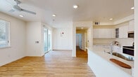 This single-story residence in Lathrop, California (95330) presents a clean, modern aesthetic defined by crisp white walls, warm light wood-tone flooring, and recessed lighting throughout. The open-concept layout connects the living and dining areas seamlessly, with a sliding glass door providing access to an outdoor space and allowing natural light to fill the interior. Ceiling fans are installed in the living area and bedrooms, contributing to both comfort and airflow.

The kitchen is thoughtfully designed with high-gloss white cabinetry extending to the ceiling, light quartz countertops, and a full suite of stainless steel appliances including a range, over-the-range microwave, and refrigerator. A peninsula offers additional counter space and casual seating potential. A stylish barn-style sliding door leads from the kitchen into a dedicated laundry area, adding a functional design detail.

The bedrooms are well-proportioned, featuring neutral walls, wood-tone flooring, ceiling fans, and windows fitted with horizontal blinds for light control. The bathroom is finished with a white vanity featuring ample cabinetry, a light-up framed mirror, and a glass-enclosed shower, all set against light flooring for a cohesive, contemporary look. The overall ambiance is bright, clean, and move-in ready.