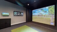 Located at 2600 Executive Dr in Venice, FL, this single-floor indoor golf simulator facility is purpose-built for immersive golf practice and entertainment. The space is divided into two distinct zones that work seamlessly together to deliver a complete simulator experience.

The simulator bay is the centerpiece of the facility, featuring a large-format projection screen that spans the full width of the striking wall, displaying highly detailed, photo-realistic golf course environments powered by an ion3 simulation system. The hitting area is outfitted with a green turf mat set into durable, multi-tone carpet flooring, providing a realistic feel underfoot. The dark ceiling and dark wall paneling surrounding the screen minimize glare and enhance image contrast, while recessed lighting keeps the space well-lit. Golf-themed framed artwork adorns the side wall, adding personality to the room. Entry to the bay is through a set of sleek double barn doors with frosted glass panels, adding a modern architectural detail.

Adjacent to the simulator bay is a comfortable lounge area with natural light filtering through horizontal blinds across multiple windows. Bar-height tables and adjustable swivel stools provide seating for spectators, while a wall-mounted television allows guests to follow the simulation action. A compact storage cabinet and overhead ceiling-mounted projector complete the functional layout of this well-appointed golf entertainment space.