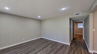 This single-floor space showcases a clean, modern aesthetic with consistent wood-style flooring running throughout every room, complemented by neutral gray and beige tones on the walls and crisp white baseboards. The open-concept layout connects the living and dining areas seamlessly, with the living room benefiting from a large window dressed with vertical blinds that invites generous natural light and outdoor views. Recessed lighting and textured ceilings add dimension to several of the rooms.

The kitchen is a functional highlight, featuring white shaker-style cabinetry, granite-look countertops with subtle speckled detailing, a stainless steel dishwasher, and a stainless steel range. An adjacent dining area with a window and direct sightlines into the kitchen makes the space ideal for everyday living and entertaining.

The bedrooms are well-proportioned and tranquil, with one featuring a built-in closet with bifold doors, a ceiling vent, and a thermostat for individual climate control. The bathroom includes a full tub-shower combination with tiled surround, a toilet, and wood-style flooring that ties the space together with the rest of the unit. Overall, the space presents a refreshed, move-in-ready environment with consistent finishes and a practical, comfortable layout.