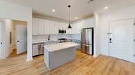 This thoughtfully designed 2-bedroom, 2-bathroom residence at 21 Locust St in Carteret, NJ offers a bright, modern living experience across a single floor. Light wood flooring flows throughout, complementing a clean, white-toned palette that gives the home a fresh and airy feel.

The open-concept living, dining, and kitchen area forms the heart of the home. The kitchen is well-appointed with white upper cabinetry, gray lower cabinets, a white subway tile backsplash, quartz countertops, stainless steel appliances including a gas range and French door refrigerator, and a central island with pendant lighting. The living and dining areas extend generously from the kitchen, bathed in natural light from large windows.

The spacious primary bedroom offers ample room and natural light, while the second bedroom features a wide window with outdoor views. Both bedrooms are served by well-finished bathrooms featuring white tile flooring, quartz vanity tops, under-mount sinks, and sleek matte black fixtures. One bathroom includes a tub-shower combo, while the other features a walk-in shower.

Additional highlights include five closets for abundant storage, an in-unit laundry area, a private balcony, and a connecting hallway that ensures a functional flow throughout the home.