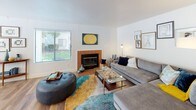 This single-story residence offers a thoughtfully designed layout across two bedrooms and two bathrooms. The living room serves as a central gathering space, highlighted by a wood-trimmed fireplace and hardwood flooring. Natural light enters through multiple windows fitted with blinds, creating a bright and welcoming atmosphere throughout.

The kitchen features white cabinetry paired with stainless steel appliances, including a full-size refrigerator, range, and microwave. A window above the counter adds natural light to the workspace. Adjacent to the kitchen, the dining area accommodates a round table setup beneath a modern multi-arm chandelier, with large windows and sliding panel curtains enhancing the space.

Both bedrooms are carpeted and include closets with built-in rods. Each room benefits from windows with outdoor views of greenery. The primary bedroom features an accent wall with textured wallpaper detailing.

The two bathrooms each include white vanity cabinetry, large mirrors, and hardwood-style flooring. One bathroom offers a shower-tub combination, while the second provides a standalone glass-enclosed shower, offering functional variety for residents.