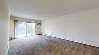 This 2-bedroom, 1-bathroom apartment in Fridley, Minnesota offers a practical and well-organized single-floor layout. The expansive living room features plush carpeting, a textured ceiling, baseboard heating, and a sliding glass door that fills the space with natural light and opens to an outdoor balcony with views of surrounding greenery. The galley-style kitchen is equipped with rich, dark wood cabinetry, a double sink, a white range, and a full-size refrigerator, with durable tile-style flooring. Two hallways connect the main living areas to the bedrooms and bathroom, providing a logical flow throughout the unit. The primary bedroom is generously sized with carpeted floors, a ceiling fan, a large window for natural light, and a wide built-in closet featuring bi-fold panel doors. The second bedroom mirrors a similar layout, also with carpet, a ceiling fan, a window, and its own closet. The full bathroom includes a tiled tub-shower combination, a vanity with dark wood cabinetry, a white countertop, and classic mosaic tile flooring. Textured ceilings and warm neutral tones carry throughout the unit, creating a consistent and understated aesthetic.