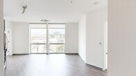 This modern two-bedroom, two-bathroom unit offers a thoughtfully designed single-floor layout with clean, contemporary finishes throughout. The open living area is defined by large floor-to-ceiling windows that flood the space with natural light and frame urban rooftop views. A cassette-style HVAC unit is integrated into the ceiling, and durable wood-style flooring runs throughout the main living areas.

The kitchen is well-appointed with two-tone cabinetry — white upper cabinets and gray lower cabinets — paired with stone-look countertops, a stainless steel sink, and a full suite of stainless steel appliances including a gas range, built-in microwave, refrigerator, and dishwasher. Track lighting above adds functional illumination.

Both bedrooms feature neutral carpet flooring and crisp white walls. The primary bedroom benefits from a large window with urban views and includes a dedicated closet with built-in shelving and hanging rods. The second bedroom is compact but functional.

The two bathrooms are finished with wood-look vinyl flooring and gray vanity cabinetry. One bathroom features a tiled tub-and-shower combination with large-format neutral gray tile and chrome fixtures, offering a clean, modern aesthetic throughout.