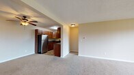 This single-floor residence offers a thoughtfully designed layout that balances functionality and comfort throughout its living spaces. The kitchen is a standout feature, showcasing rich medium-toned wood cabinetry, dark granite countertops, tile flooring, and a full suite of stainless steel appliances including an electric range, over-the-range microwave, and refrigerator. A breakfast bar provides a convenient transition into the adjacent living area. The open-concept living space is generously sized, finished with neutral-toned wall-to-wall carpeting and a ceiling fan, creating a bright and airy atmosphere. A column detail adds architectural interest and helps delineate the kitchen from the main living area. The bedroom features plush carpeting, a window that brings in natural light, and a spacious walk-in closet with built-in wire shelving on both sides, offering exceptional storage. The bathroom is well-appointed with tile flooring, beige wall tile surrounding the soaking bathtub and shower combination, a wood vanity, and chrome grab bars for added accessibility and safety. Throughout, the space maintains a consistent, clean aesthetic with textured ceilings and warm neutral tones.