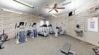 Located at 100 Lisbon Ct in Virginia Beach, VA, this fitness center offers a well-equipped workout space designed to support a well-rounded exercise routine. The single-room facility is defined by its distinctive stacked-stone accent walls in neutral tones of gray, beige, and white, lending the space a modern yet welcoming aesthetic that sets it apart from a typical gym environment.

The flooring throughout is a smooth, wood-look surface that is easy to maintain and visually cohesive. Ceiling fans are installed throughout the space, ensuring consistent air circulation during workouts. Overhead linear lighting supplements natural light from multiple windows fitted with blinds, creating a bright and functional atmosphere.

The cardio section is well-stocked with treadmills, elliptical trainers, a stair climber, and a recumbent bike, providing a variety of options for cardiovascular exercise. A cable cross machine serves as the centerpiece of the strength training area, complemented by a full rack of dumbbells in graduated weights and a workout bench for versatile strength training. Stability balls and medicine balls round out the functional fitness offerings.

Additional amenities include a wall-mounted flat-screen television for entertainment during workouts, a drinking fountain near the exit door, and large mirrors that enhance the sense of openness. The space is efficiently organized to maximize usability within its footprint.