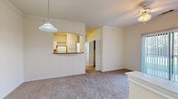 This single-floor, 1-bedroom, 1-bathroom unit offers a thoughtfully organized layout that maximizes its compact footprint. The living area is carpeted and filled with natural light from a sliding glass door that opens to an outdoor patio, providing pleasant outdoor views. A ceiling fan with light fixture adds both comfort and functionality to the space. Crown molding along the ceiling lends a refined touch throughout the main living area.

The kitchen is accessed via a charming arched pass-through opening framed by a dark-toned countertop bar, creating a semi-open connection to the living space. The kitchen itself features white cabinetry, a built-in wine rack, and white appliances, all illuminated by a ceiling-mounted light fixture.

The bedroom is a comfortable, carpeted room benefiting from natural light through a window with blinds and is equipped with its own ceiling fan. Two closets serve the unit, including a generously sized walk-in closet outfitted with wire shelving for practical storage.

The bathroom features wood-look flooring, a full tub-shower combination with tiled surround, a toilet, and a wide vanity with a large mirror, all finished in a clean, neutral palette that contributes to the unit's bright and airy overall ambiance.